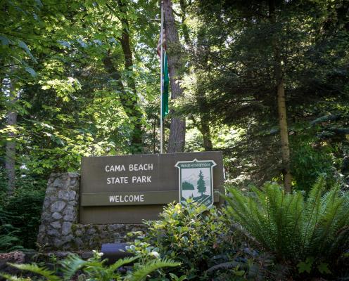 Cama Beach State Park Sign surrounded by lush green forest plants and trees. 