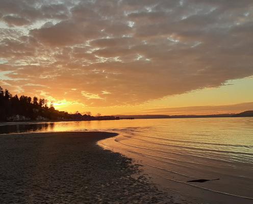 Tide washing over sand, orange sunset with clouds.