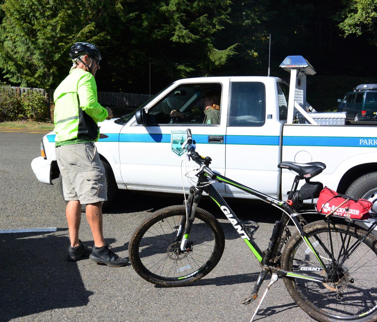 Bicyclists converse with park staff, who is sitting in a ranger truck.