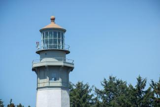 The top portion of Grays Harbor Lighthouse with evergreens and a blue sky in the background