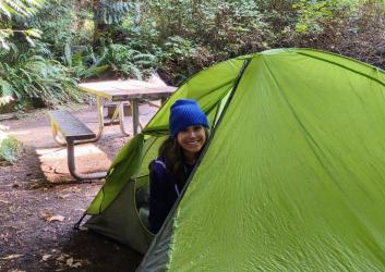 Camper peaks out of a green tent at a camping spot