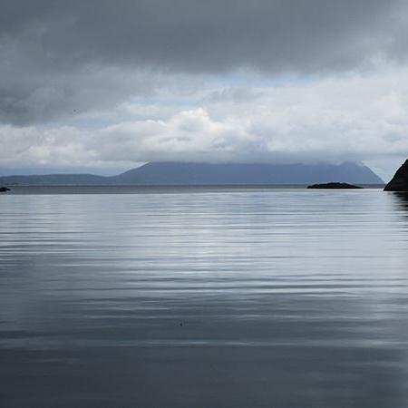 calm water leading out to island shrouded in clouds