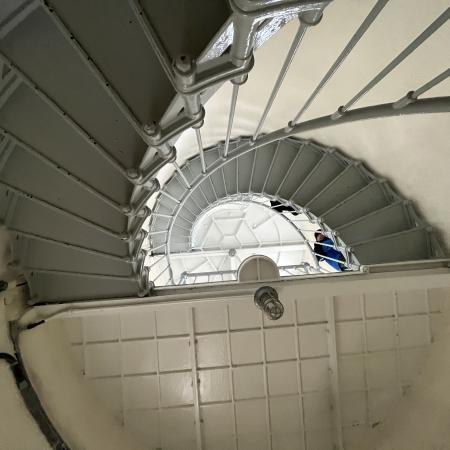 Looking up the white interior of the lighthouse, the grey stair spiral up as guests walk up them.