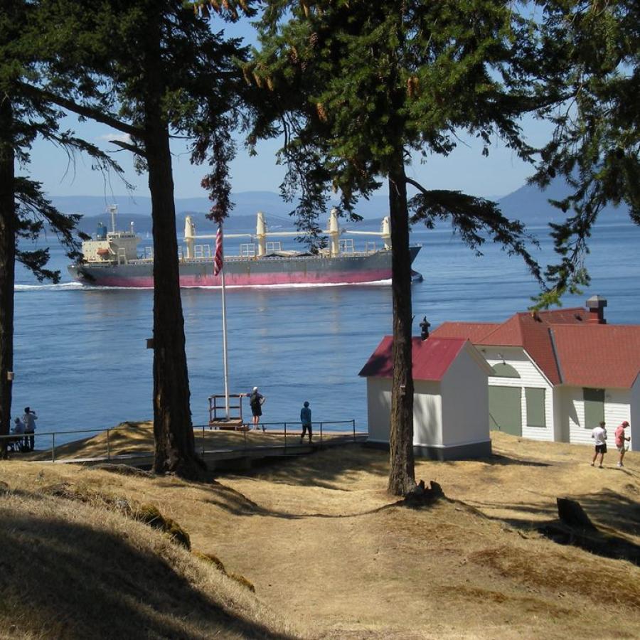 island boat house in white with red roof looking out to the waterway with large ship passing