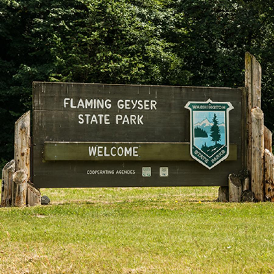 A wooden sign reading Flaming Geyser State Park Welcome and bearing the Washington State Parks Shield