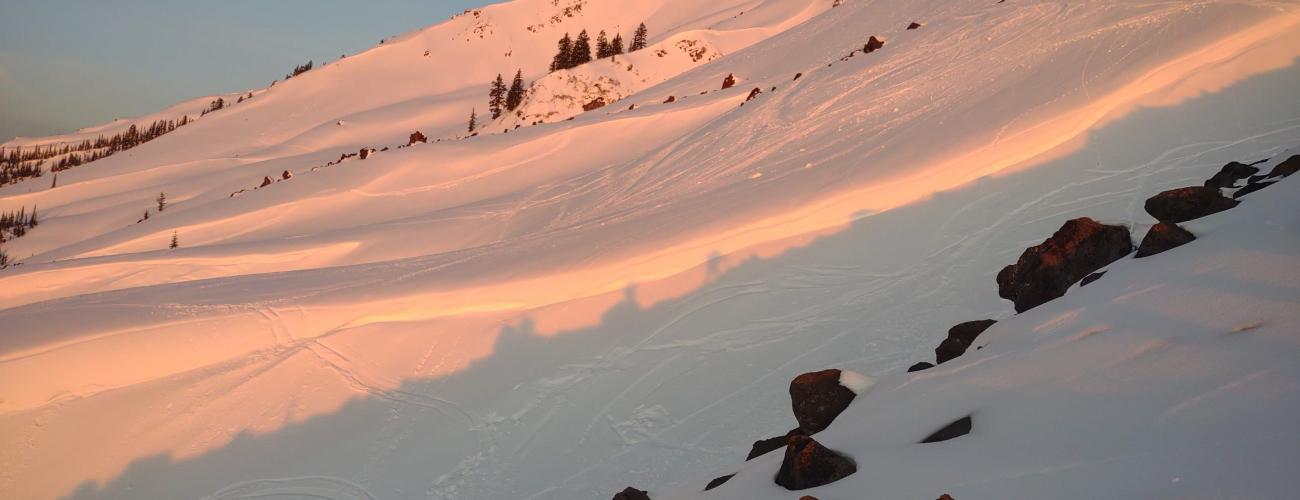 Pink and orange reflection of sunrise on a snowy mountain slope