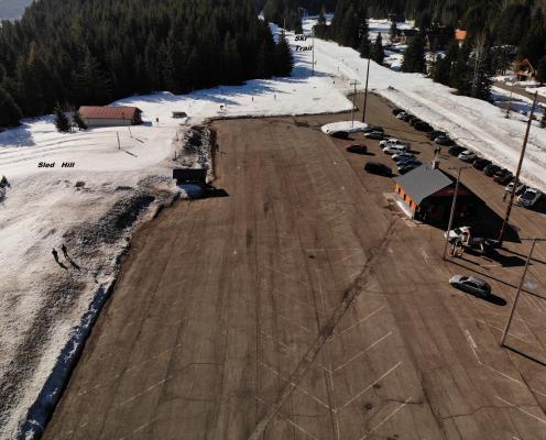A large, dry, and cleanly plowed parking lot with a small building, next to a sled hill and ski trail with deep snow.