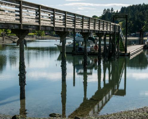 A dock is reflected in calm water. A boat sits tied to the end of the dock.