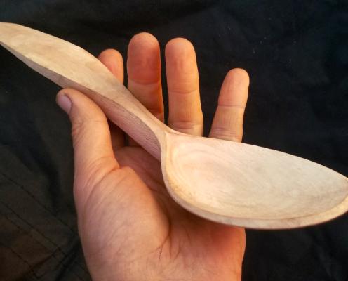 A hand holding a handmade wooden spoon