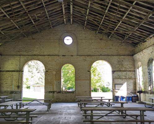 Inside a large brick and wooden hall with arched entrance and windows with no glass