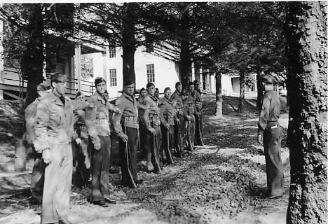 A black and white photograph of soldiers standing in a line in front of their barracks