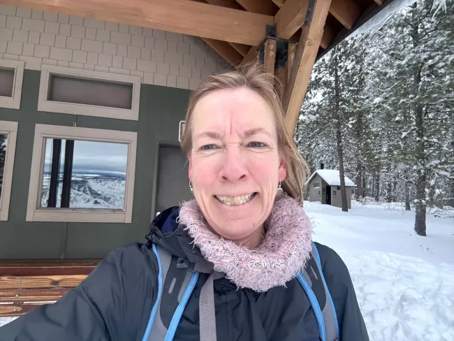 W woman smiles in front of a building on a winter day. there is snow on the ground.