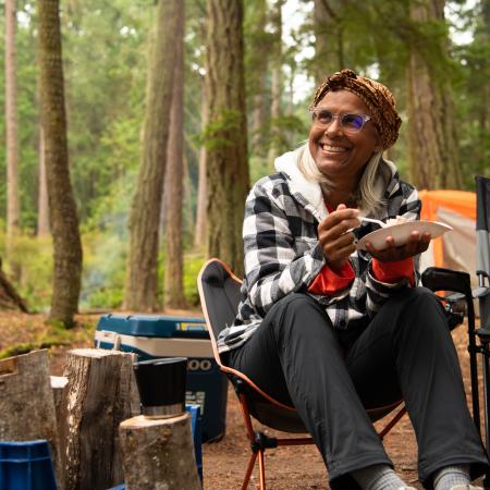 Woman eating by campfire.