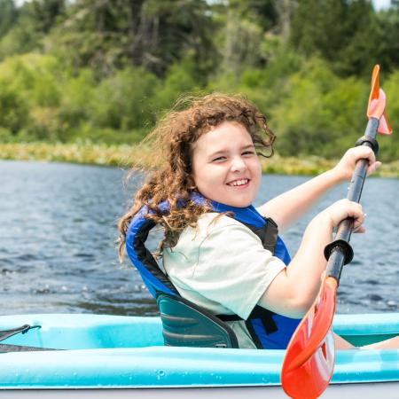 a young girl kayaking on a lake while wearing a life jacket