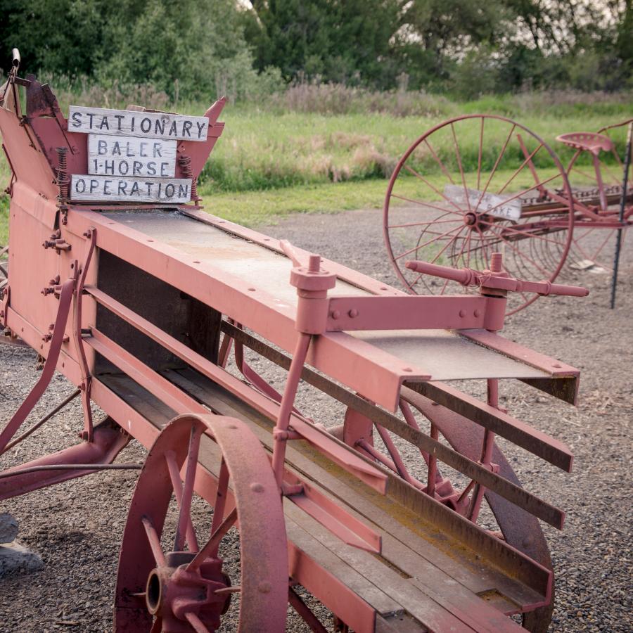 One horse hay baler early to mid 1900s sitting on top gravel as a display as a display of early farming equipment. A sit behind horse pulled rake is behind the baler also on dispay.