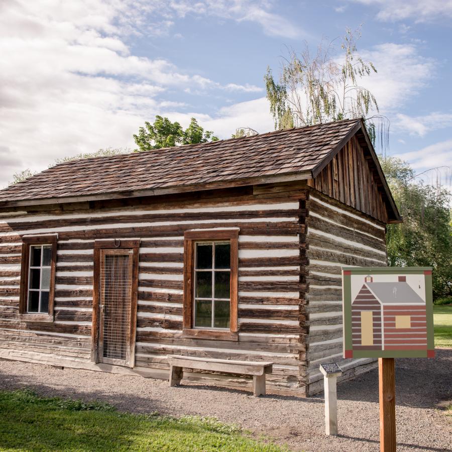 A one room K though 12 wood structure schoolhouse in front of green leafy tress and white clouds against blue sky