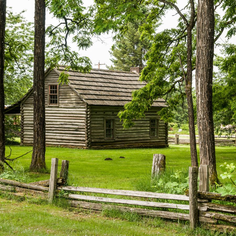 old world cabin of wood surrounded by green grass and wood rail fence