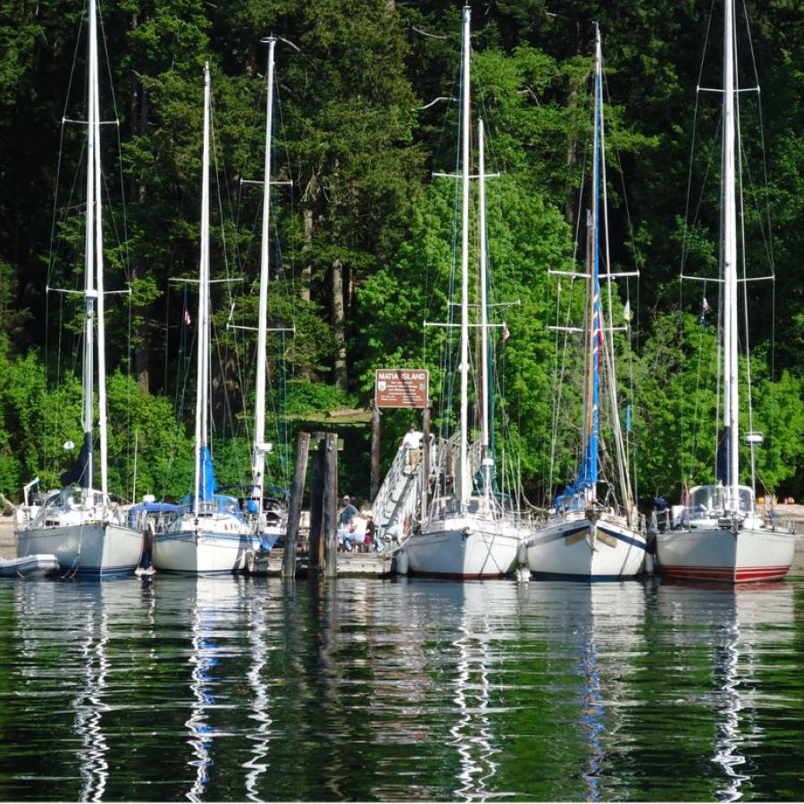 five sail boats with tall masts facing outward docked on walkway