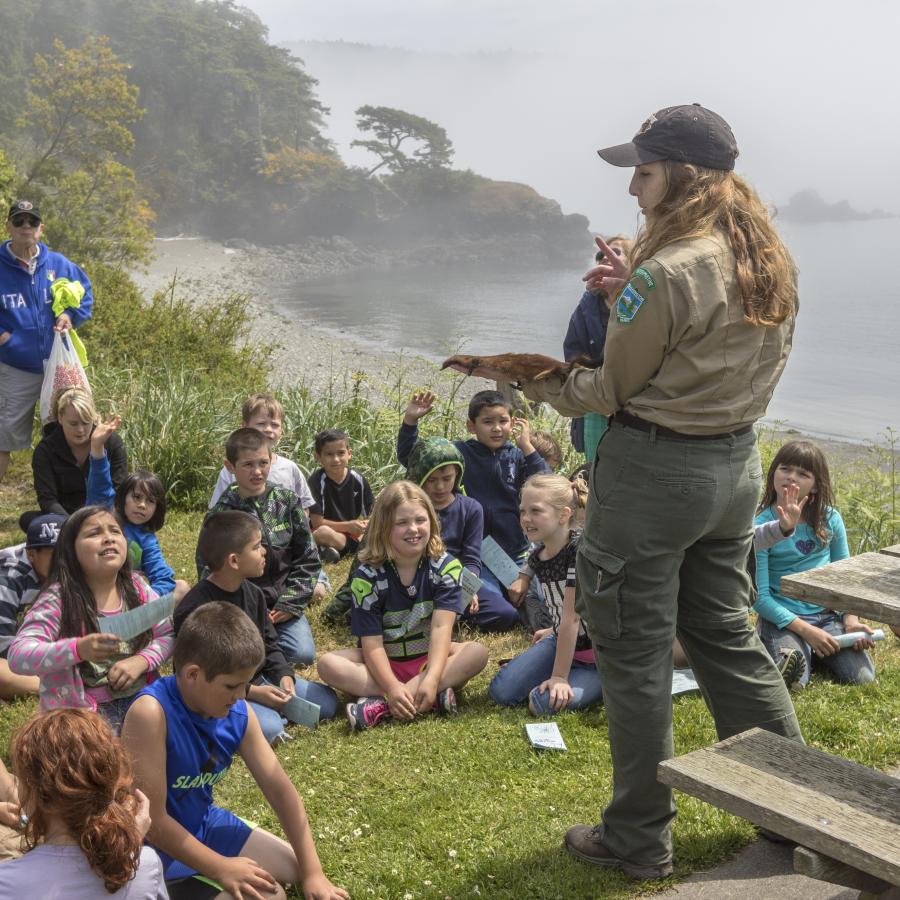 Group of young children sitting on the grass listen to a ranger talk