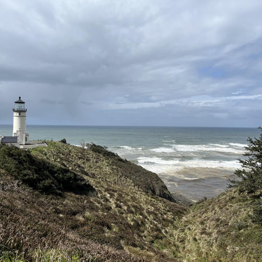 Standing on a rocky shore, looking towards the ocean, North Head Lighthouse is white against a stormy grey sky.