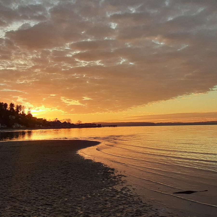 Tide washing over sand, orange sunset with clouds.