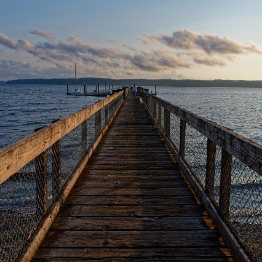 View looking straight down the dock. Blue water and colorful clouds in the distance.