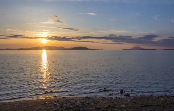 On the beach at the water's edge, a blue and yellow sunset with a streak of clouds above islands in the background.