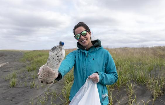 Volunteer in sunglasses collecting trash on a beach.